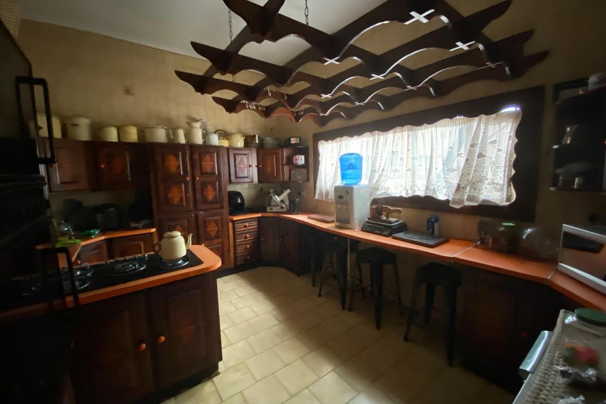 A dated kitchen featuring dark wood cabinetry, integrated cooktop, and a unique overhead wooden lattice structure, offering a traditional aesthetic with ample counter space.