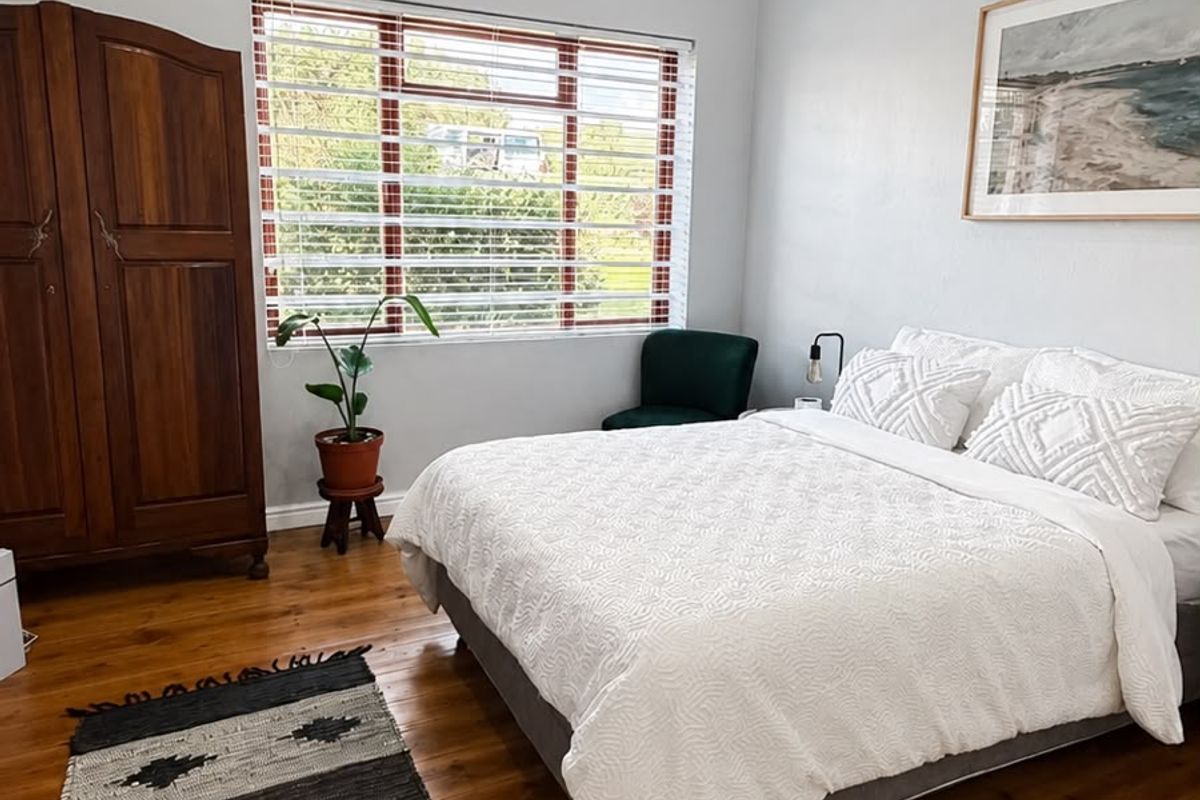 A bright and spacious bedroom featuring polished hardwood flooring, high ceilings with recessed lighting, and a large window with venetian blinds.