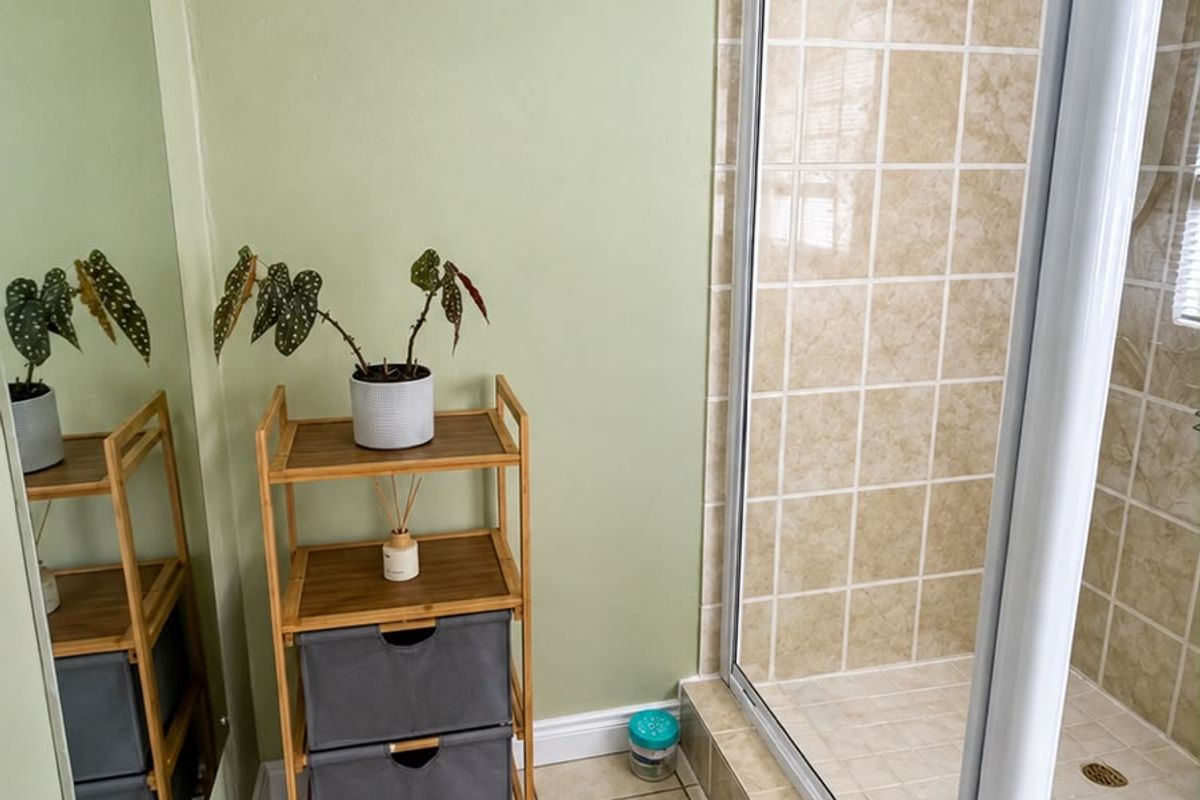 A functional bathroom featuring a tiled shower enclosure, neutral floor tiles, and a large wall-mounted mirror with light green wall finishes.