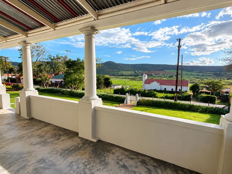 Spacious covered patio featuring classical columns and concrete flooring, offering expansive views of the surrounding landscape and countryside.