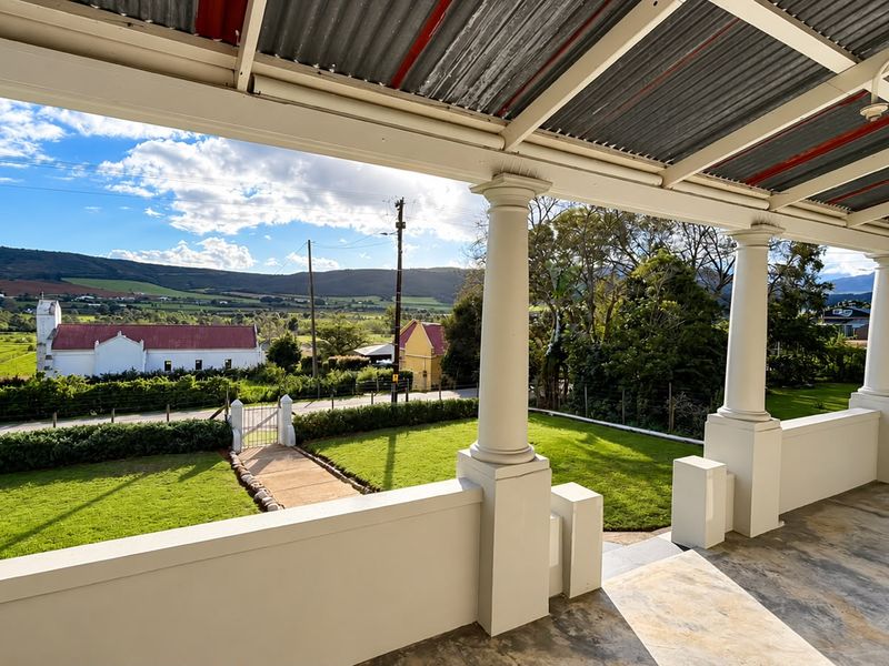 A spacious covered veranda featuring classical columns and a masonry balustrade, offering expansive views over the garden and surrounding rural landscape.