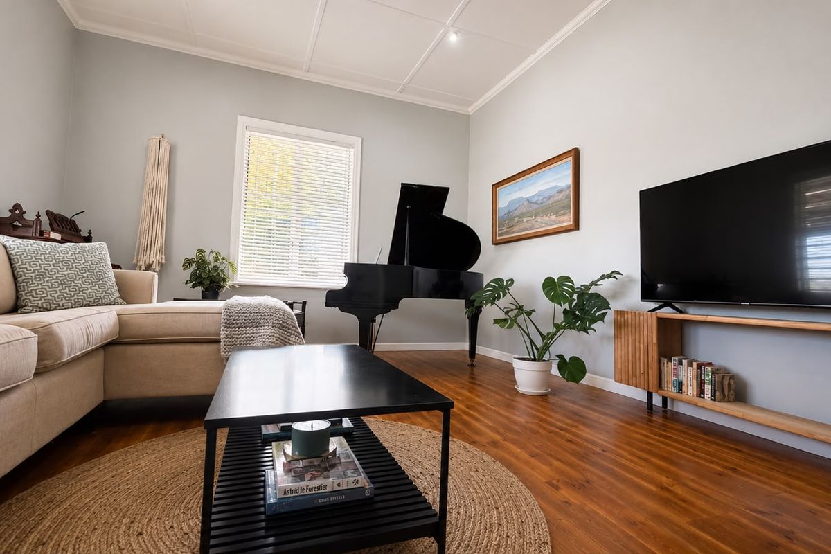 A well-maintained living room featuring polished hardwood flooring, classic ceiling paneling, and natural light through venetian blinds.