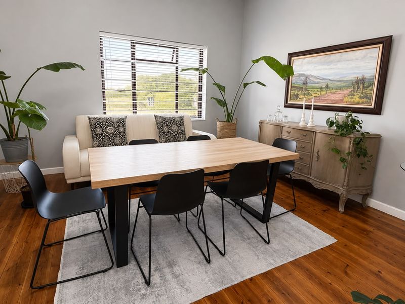 A well-maintained dining room featuring warm timber flooring, neutral wall tones, and a large window providing natural light and exterior views.