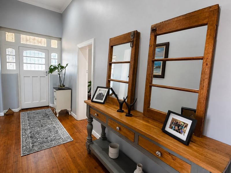 A bright and welcoming entrance hall featuring polished timber flooring, high ceilings with coved cornicing, and a classic panelled front door with fanlight.