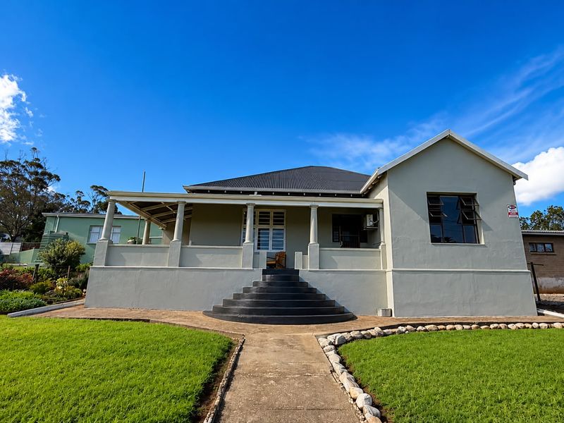 Front elevation of a well-maintained house featuring a covered veranda, concrete stairs, and a neat front lawn with a paved pathway.