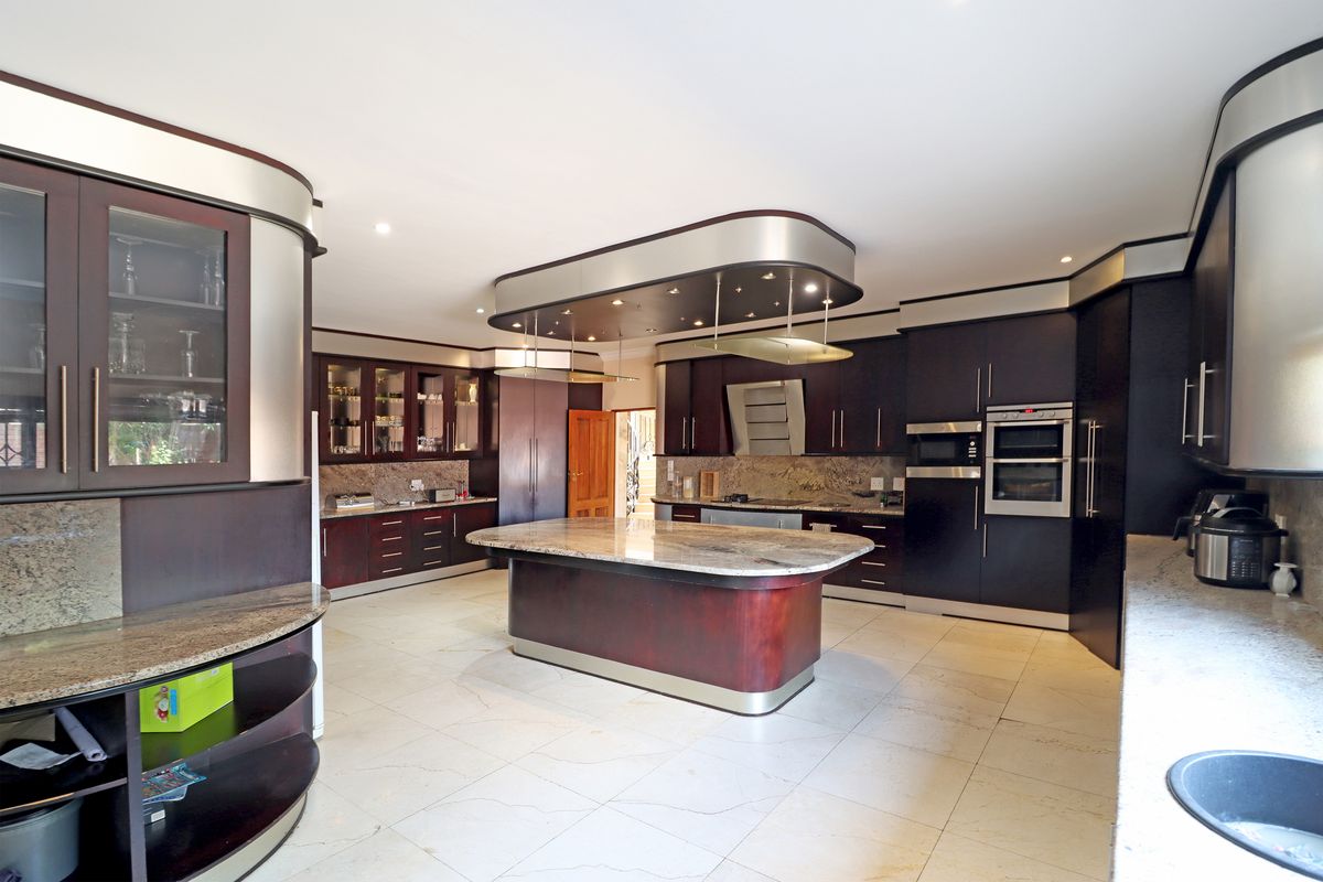 Spacious kitchen featuring dark custom cabinetry, granite countertops, a central island, and integrated appliances with modern recessed lighting.
