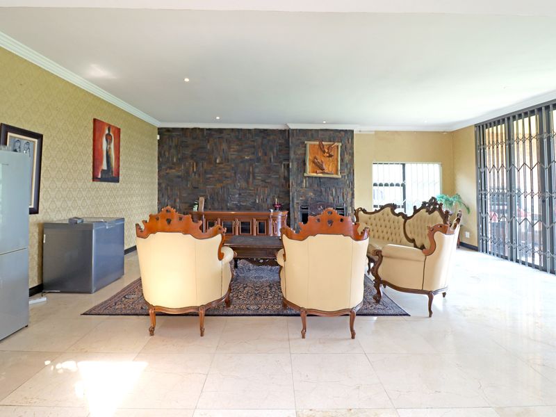 Spacious living room featuring tiled flooring, a prominent stone-clad fireplace, and large security gates leading to the exterior.