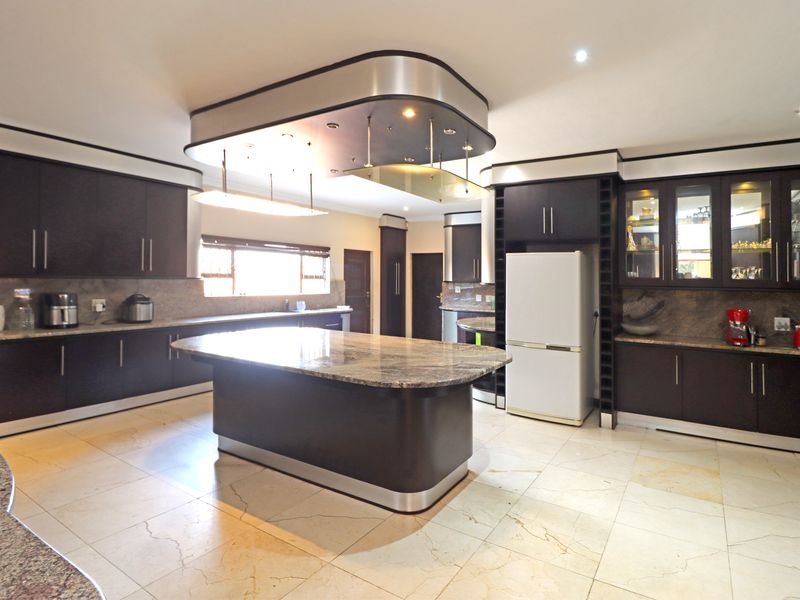 Spacious modern kitchen featuring dark cabinetry, granite countertops, a central island, and a unique suspended ceiling feature with integrated lighting.