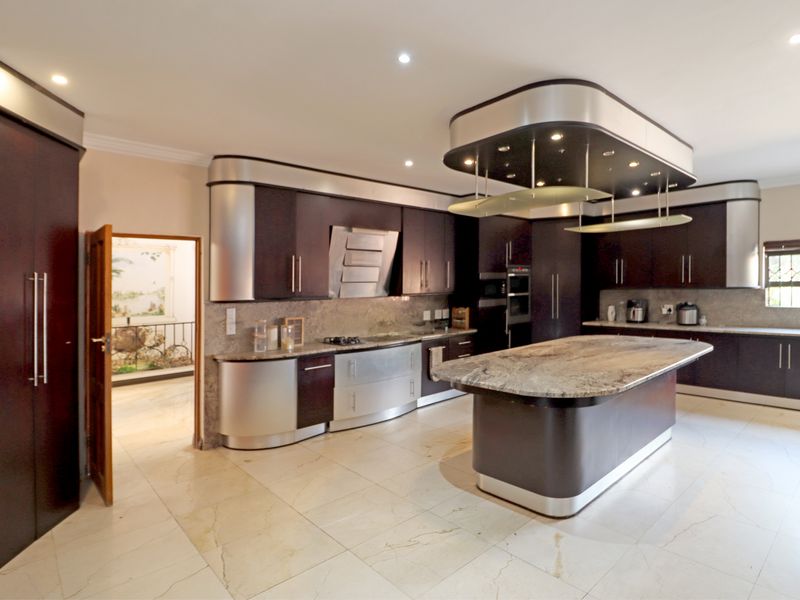 Spacious modern kitchen featuring dark cabinetry, a large stone-topped island, integrated appliances, and recessed ceiling lighting.