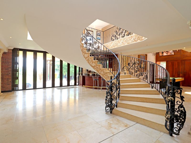 Grand entrance hall featuring a sweeping curved stone staircase with ornate wrought iron railings, marble flooring, and decorative columns.