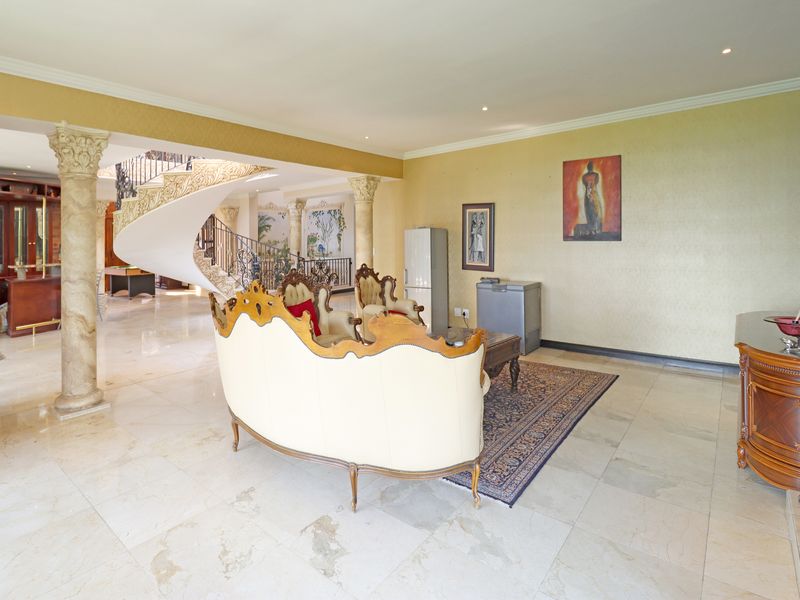 Spacious living area featuring elegant marble flooring, decorative stone columns, and a grand spiral staircase leading to the upper level.