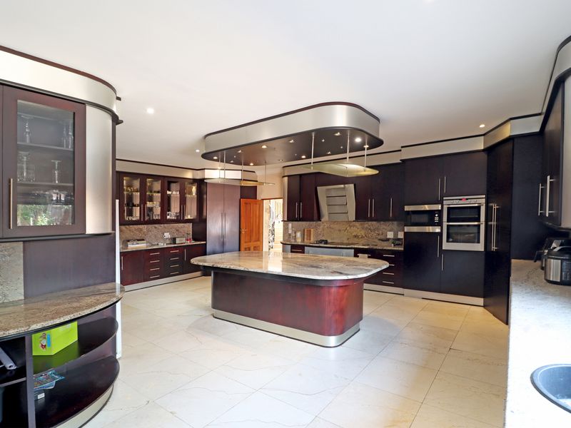 Spacious kitchen featuring dark custom cabinetry, granite countertops, a central island, and integrated appliances with modern recessed lighting.