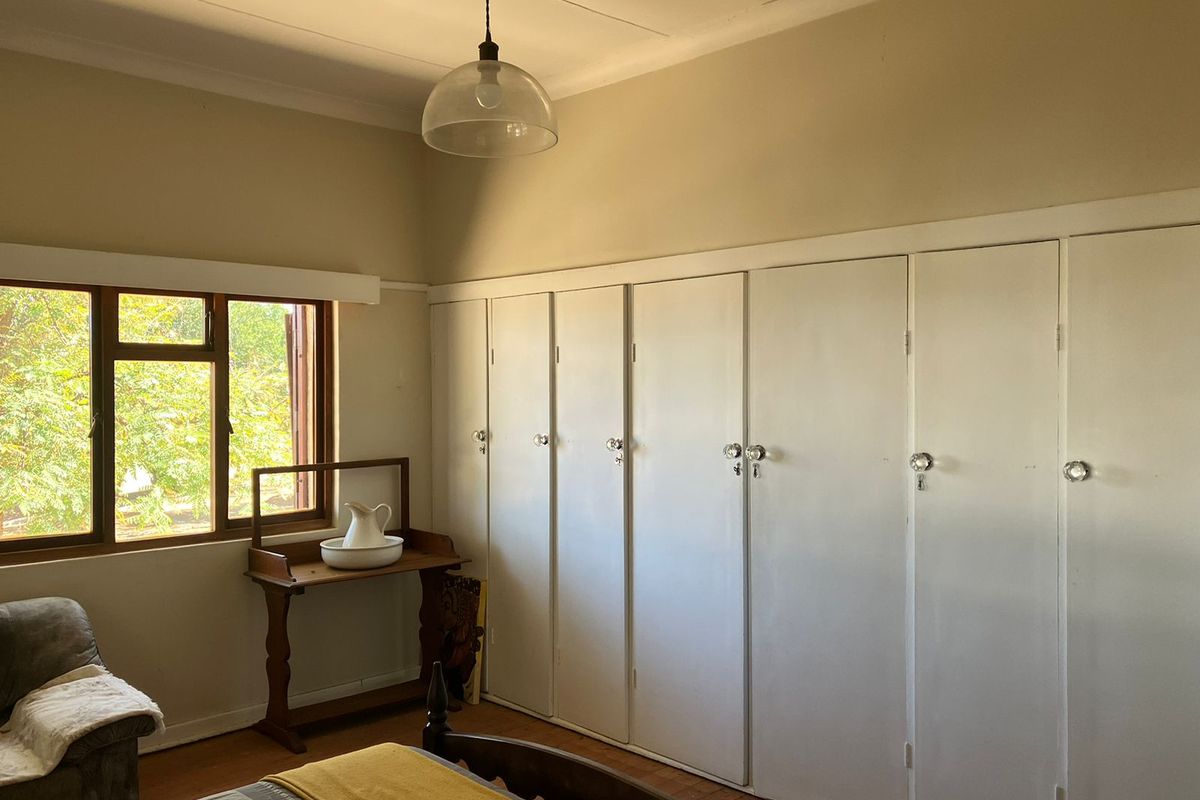 A bedroom featuring extensive built-in cupboards, timber flooring, and a large window providing natural light and garden views.