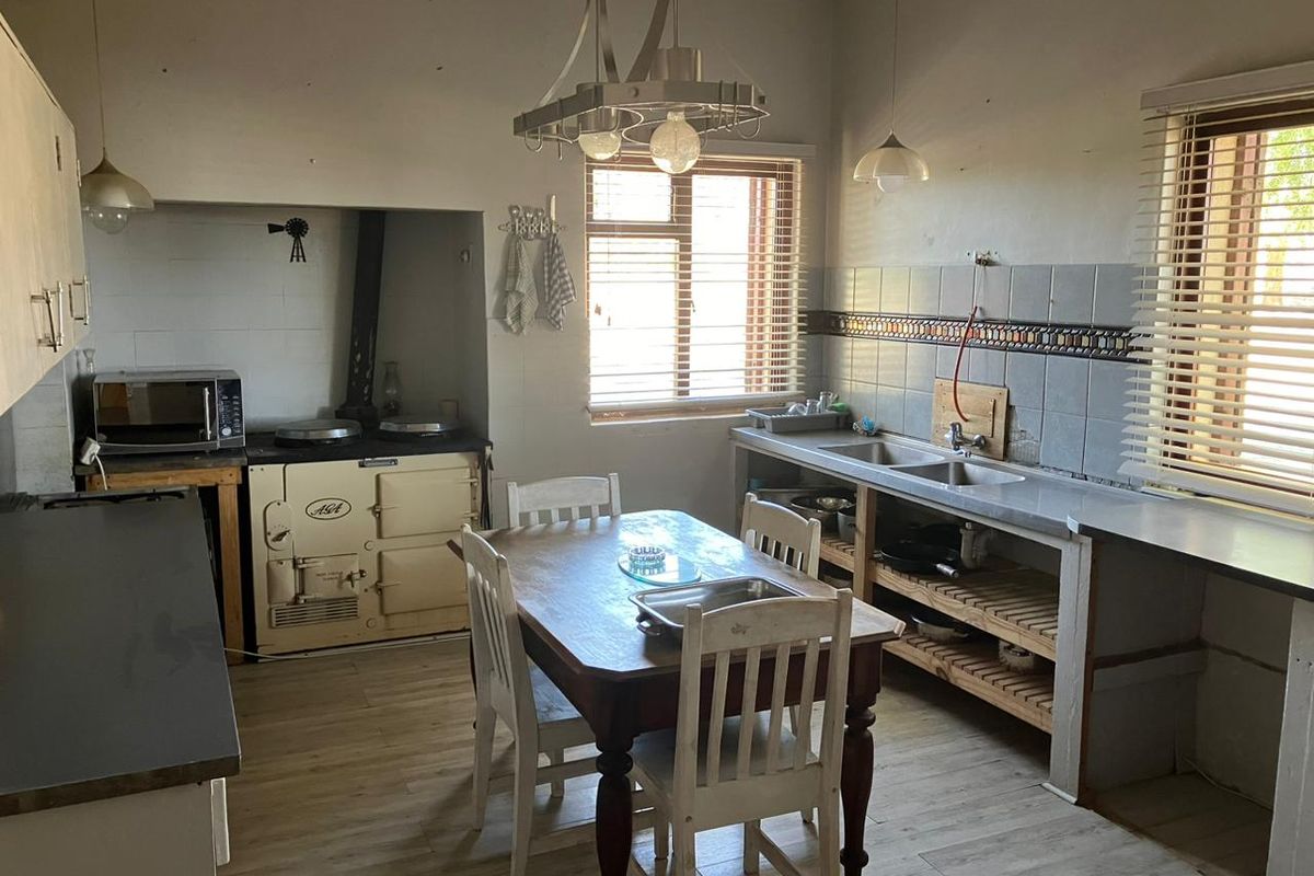 A rustic farmhouse kitchen featuring a classic AGA stove, double basin sink, and timber shelving, offering a traditional country aesthetic with potential for modernization.