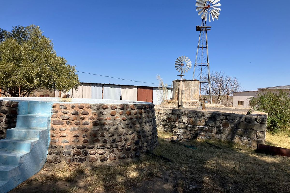 Farm exterior featuring a traditional windmill, stone water reservoir with steps, and corrugated metal outbuildings on the property grounds.