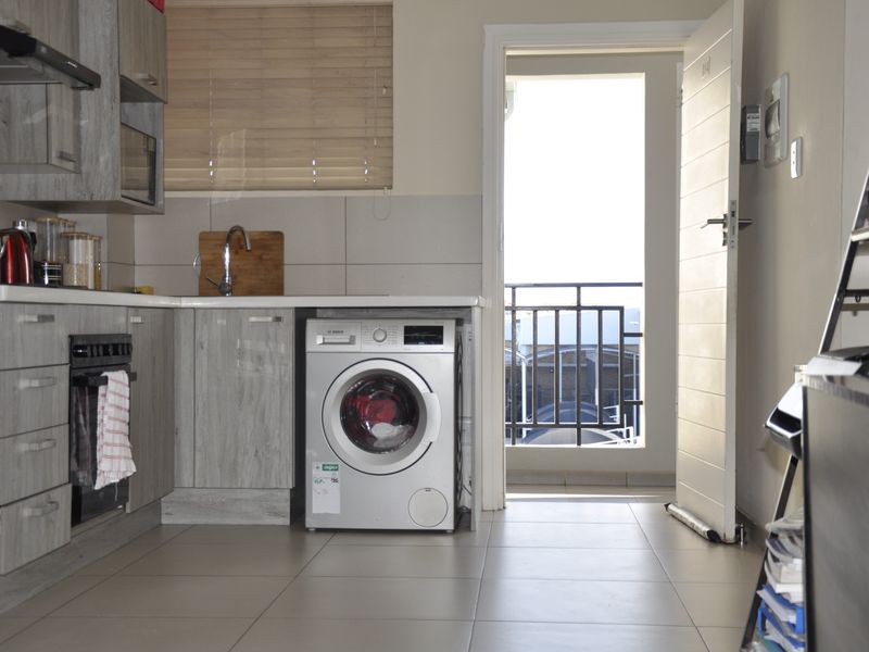 Modern kitchen featuring grey wood-look cabinetry, built-in oven, extractor fan, and integrated washing machine, with direct access to a balcony.