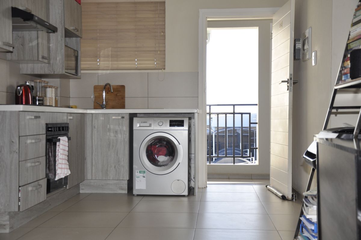 Modern kitchen featuring grey wood-look cabinetry, built-in oven, extractor fan, and integrated washing machine, with direct access to a balcony.