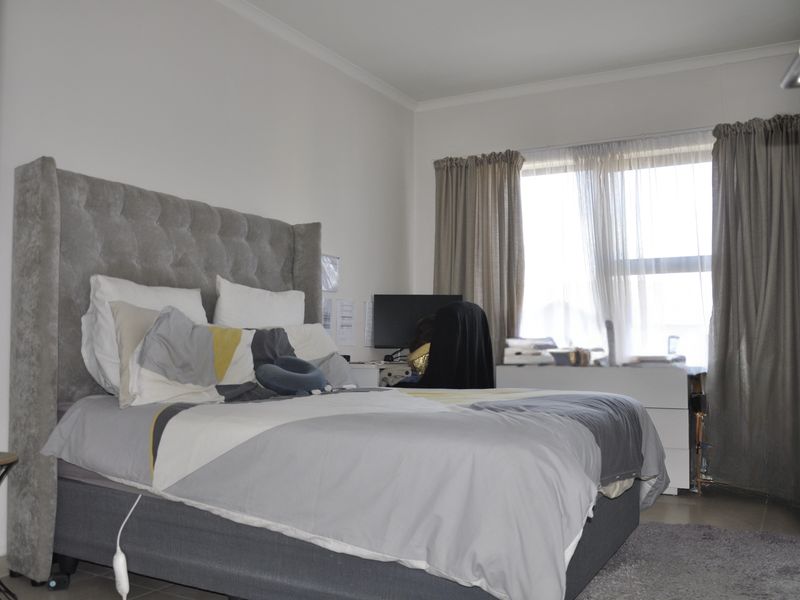 A well-lit bedroom featuring neutral wall finishes, tiled flooring, and large windows with installed curtain rails.