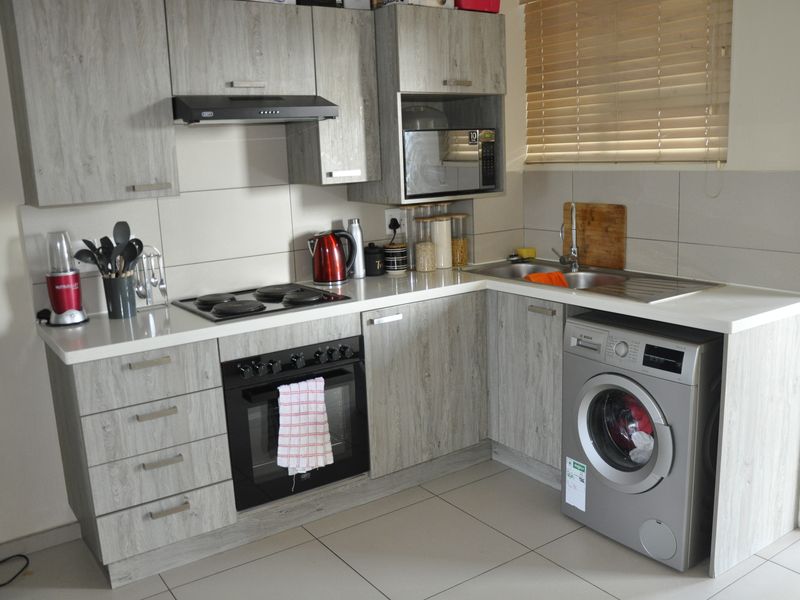 Modern kitchen featuring light wood-grain laminate cabinetry, built-in oven, electric hob, extractor fan, stainless steel sink, and an integrated washing machine.