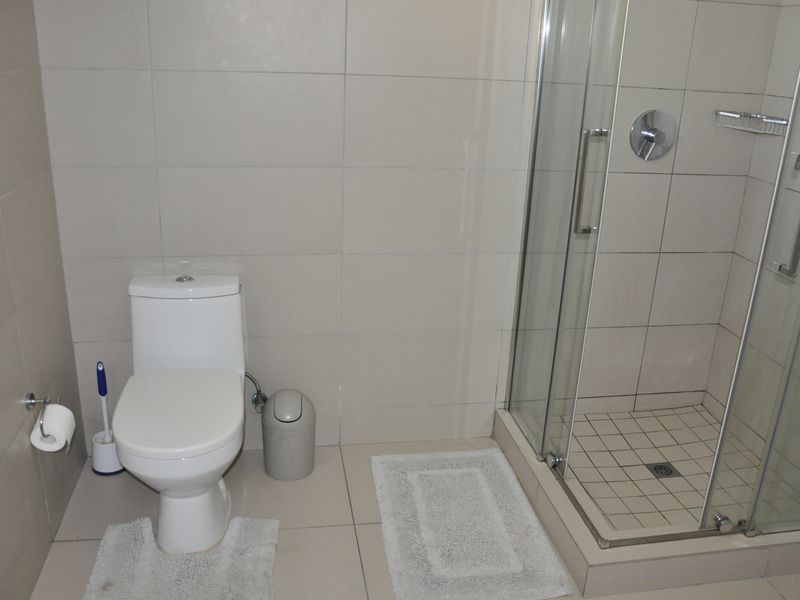 A functional bathroom featuring a glass-enclosed shower, modern toilet, and neutral wall and floor tiling throughout.
