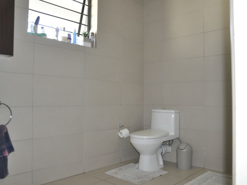 A functional bathroom featuring neutral wall and floor tiles, a standard toilet, and a window with security bars.
