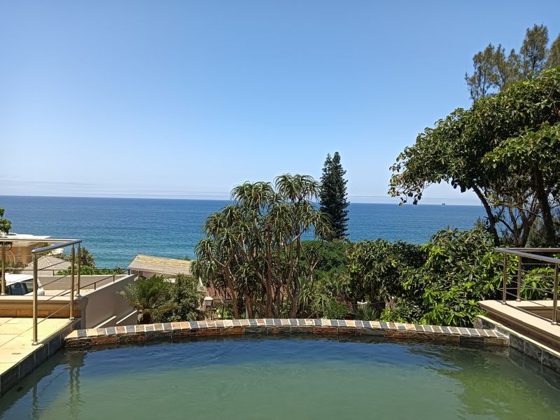 An elevated swimming pool area featuring stone coping and stainless steel balustrades, offering expansive ocean views.