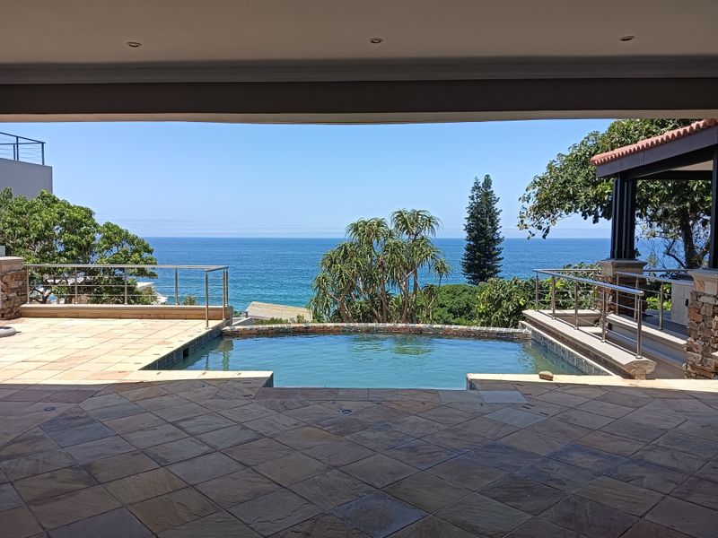 An outdoor patio area featuring a swimming pool with stone tiling, stainless steel balustrades, and expansive ocean views.