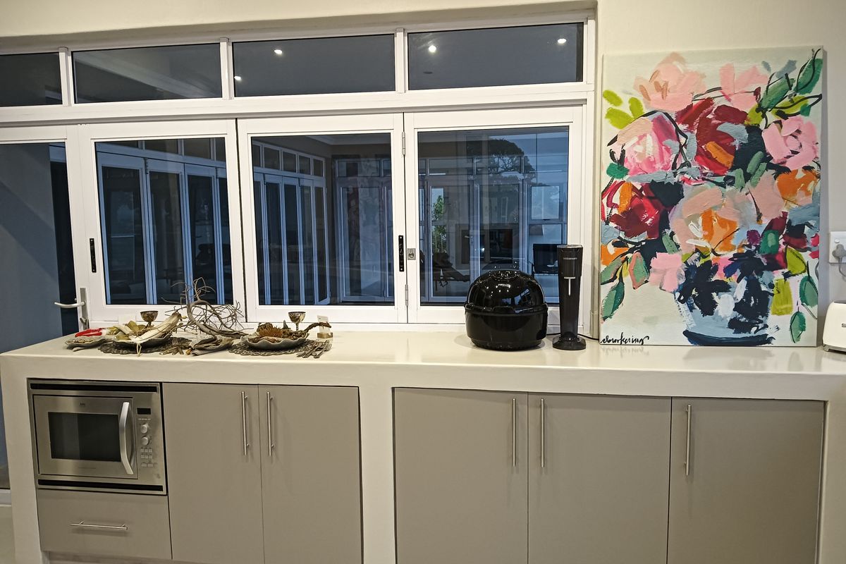A modern kitchen area featuring sleek grey cabinetry, a smooth stone countertop, and a built-in microwave, set against a large multi-pane window.