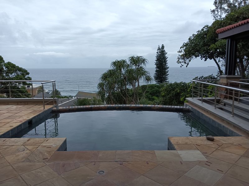 An outdoor swimming pool area featuring stone paving and stainless steel balustrades, offering expansive ocean views.