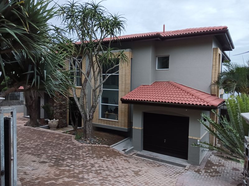 Front elevation of a modern two-story house featuring a tiled roof, brick accents, large feature window, and an integrated garage with a paved driveway.