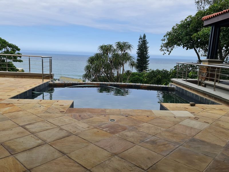 Outdoor pool area featuring stone paving, stainless steel balustrades, and expansive ocean views.