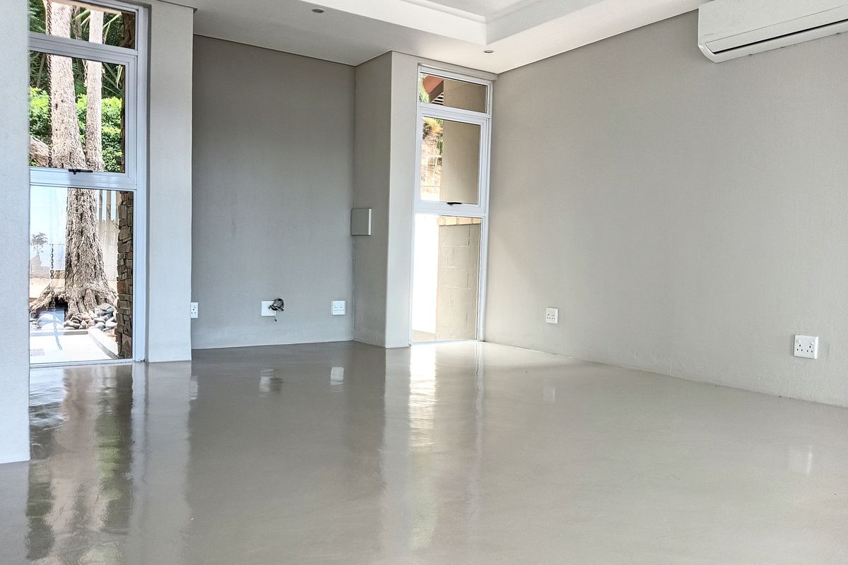 A bright, empty living area featuring polished concrete floors, recessed ceiling lighting, and a wall-mounted air conditioning unit with large windows.
