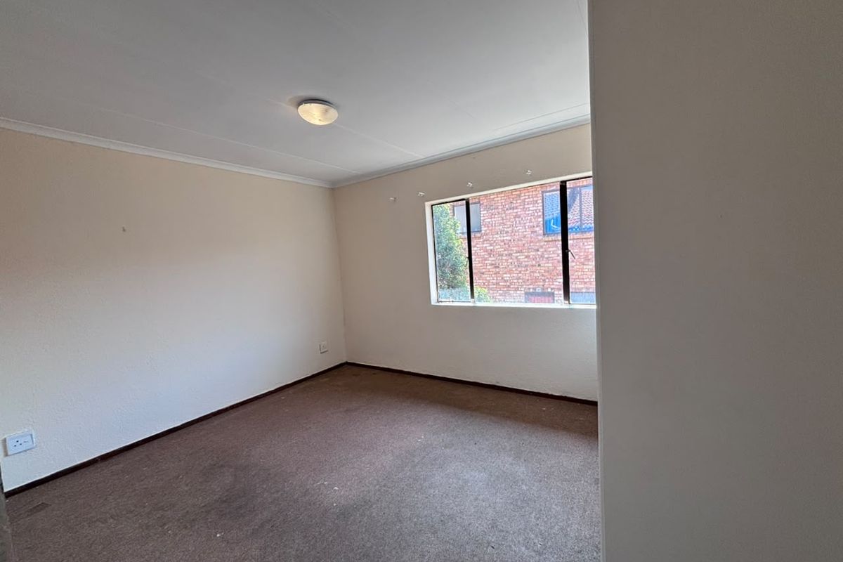 A vacant bedroom featuring neutral walls, carpet flooring, and a window with an aluminum frame, offering a blank canvas for personalization.