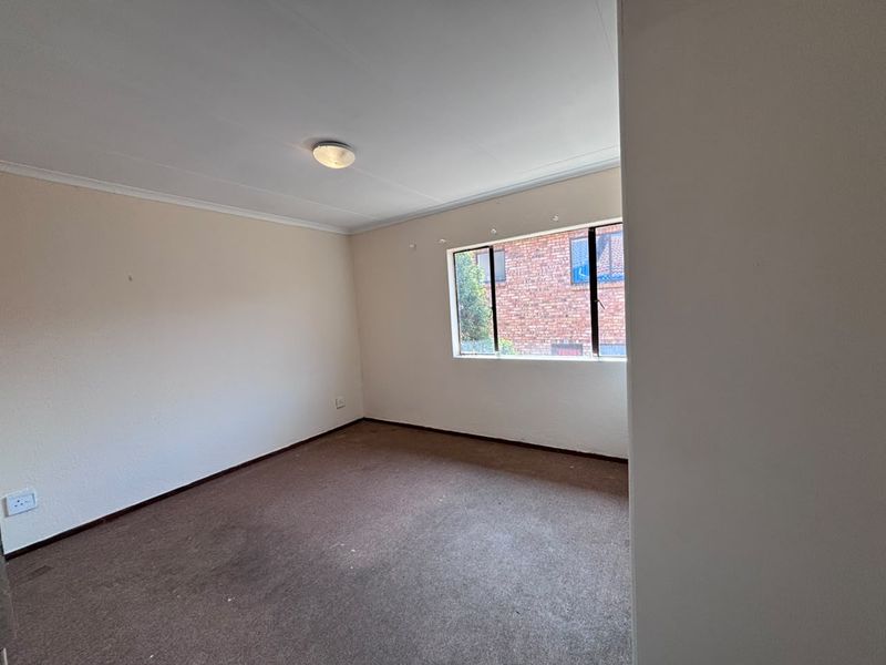 A vacant bedroom featuring neutral walls, carpet flooring, and a window with an aluminum frame, offering a blank canvas for personalization.