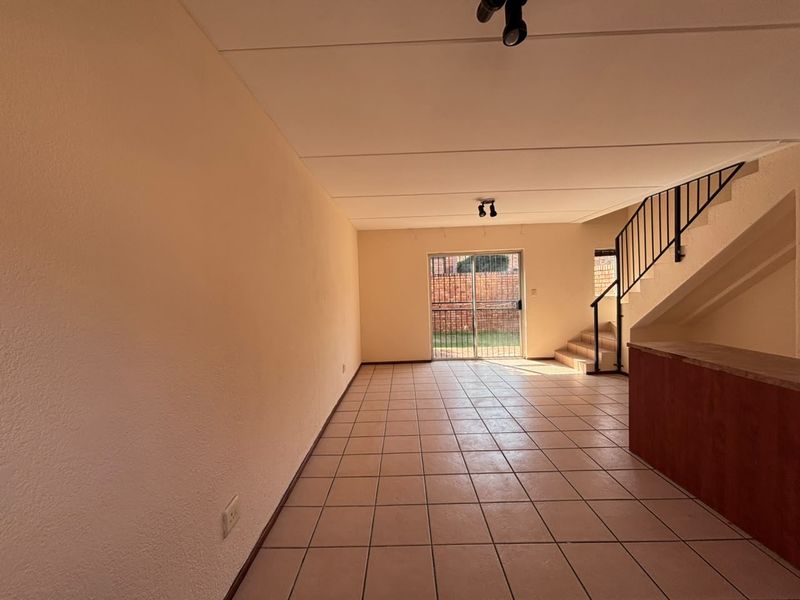 An empty open-plan living area featuring tiled flooring, a staircase with a metal balustrade, and a sliding glass door leading to the rear exterior.