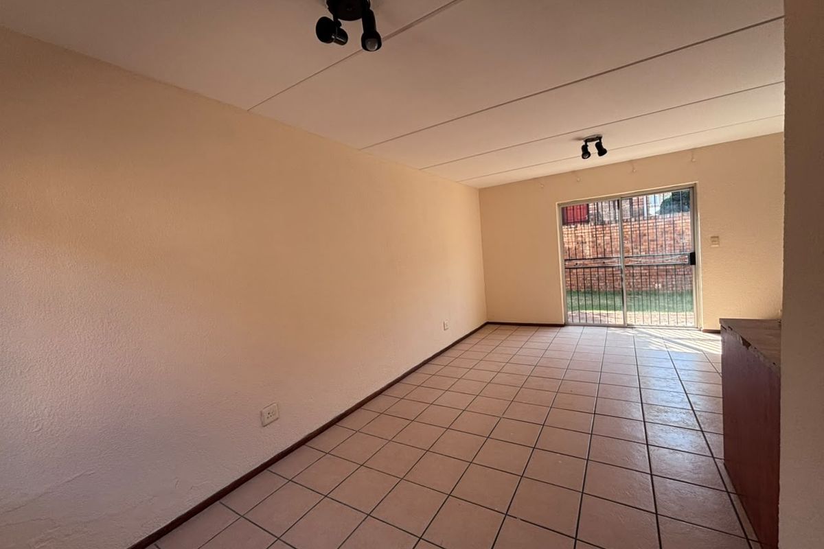 An empty living room featuring tiled flooring, spotlight fixtures, and a sliding glass door providing access to the rear exterior.