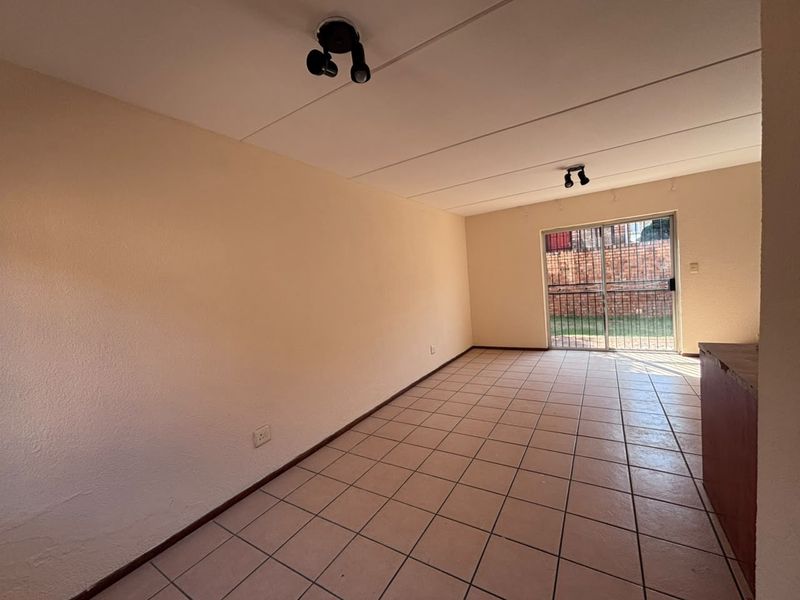 An empty living room featuring tiled flooring, spotlight fixtures, and a sliding glass door providing access to the rear exterior.