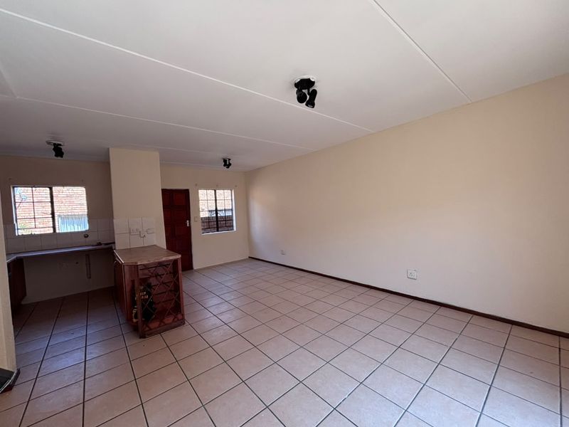 Spacious open-plan living area featuring tiled flooring, neutral walls, and a functional kitchen corner with built-in cabinetry and a wine rack.