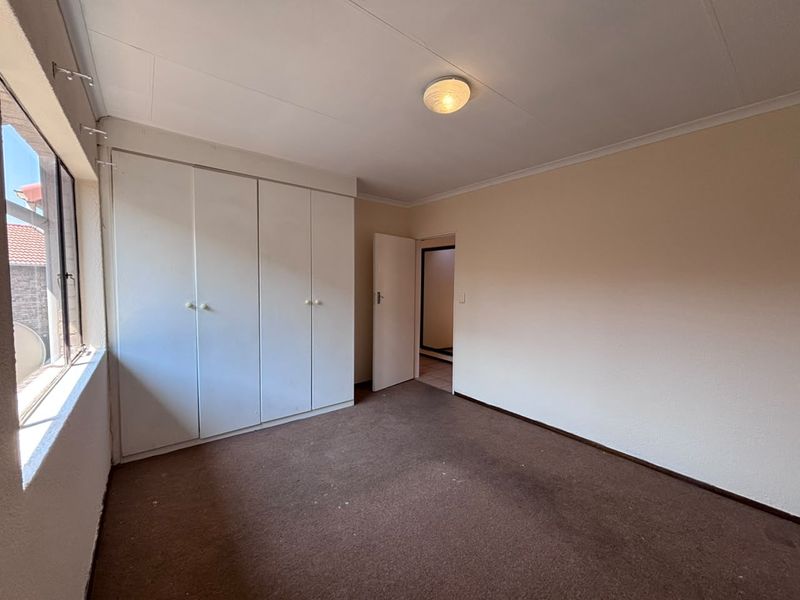A vacant bedroom featuring built-in cupboards, neutral wall finishes, and carpet flooring, offering a blank canvas for potential updates.