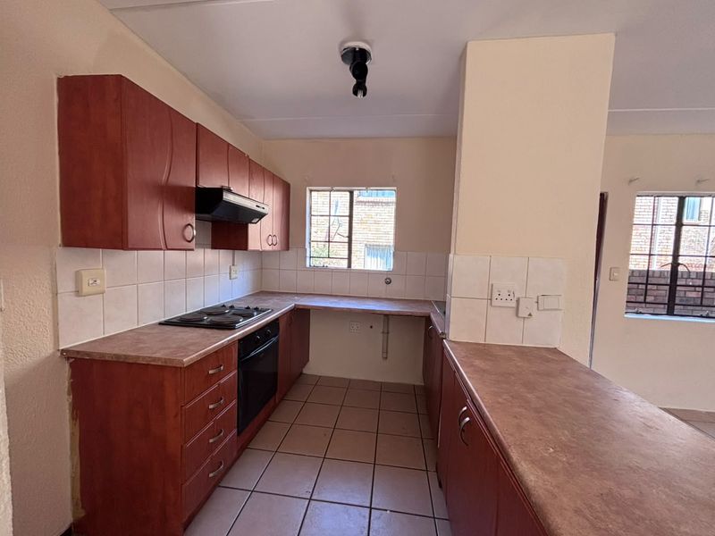 A functional kitchen featuring built-in wooden cabinetry, laminate countertops, an electric hob, and an oven, with tiled flooring and splashbacks throughout.