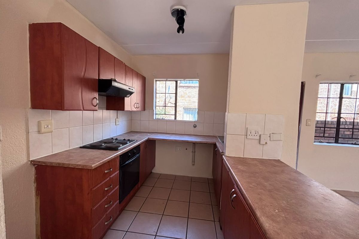 A functional kitchen featuring built-in wooden cabinetry, laminate countertops, an electric hob, and an oven, with tiled flooring and splashbacks throughout.
