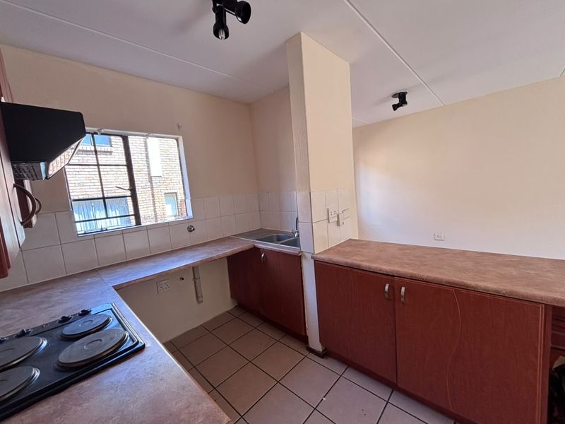 A functional kitchen featuring built-in cabinetry, laminate countertops, a stainless steel sink, and an integrated electric hob with an extractor fan.