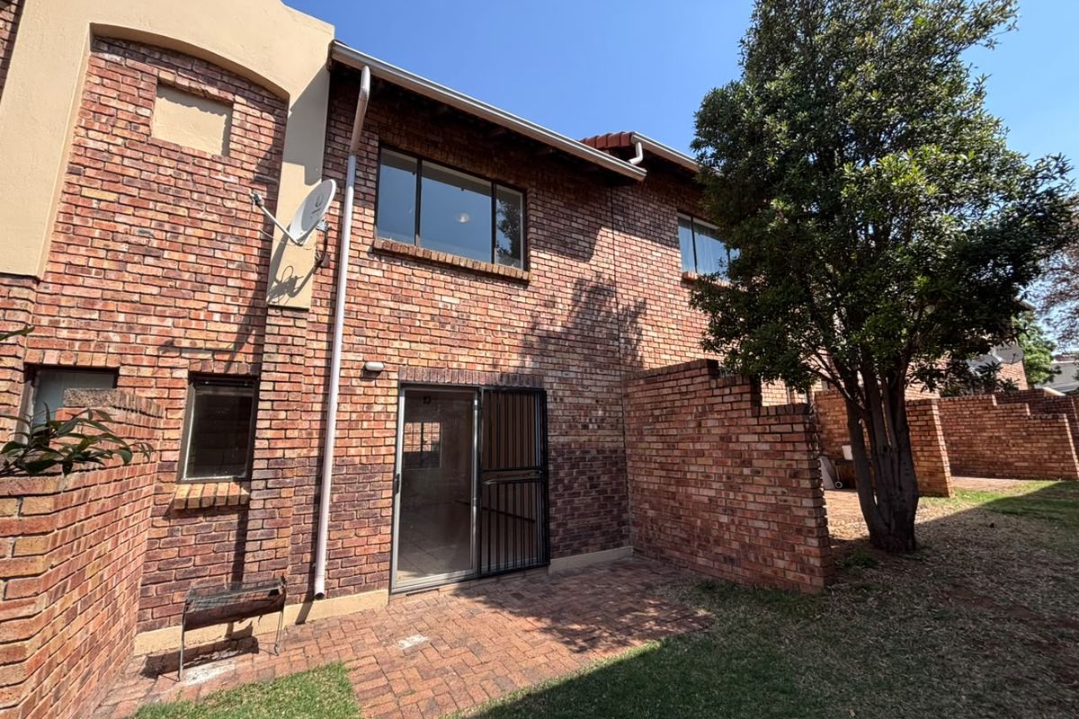 Rear view of the townhouse featuring a face brick facade, a paved patio area, and a sliding glass door with a security gate.