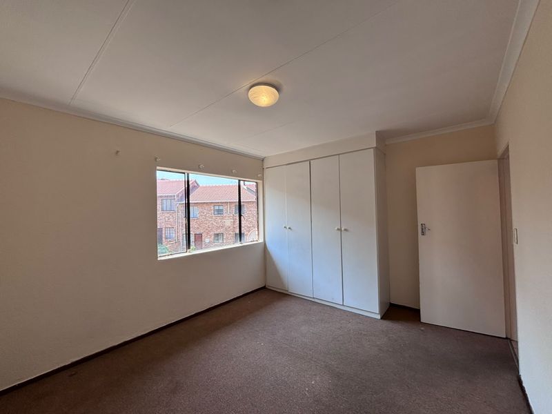 A vacant bedroom featuring built-in cupboards, carpeted flooring, and a large window providing natural light.