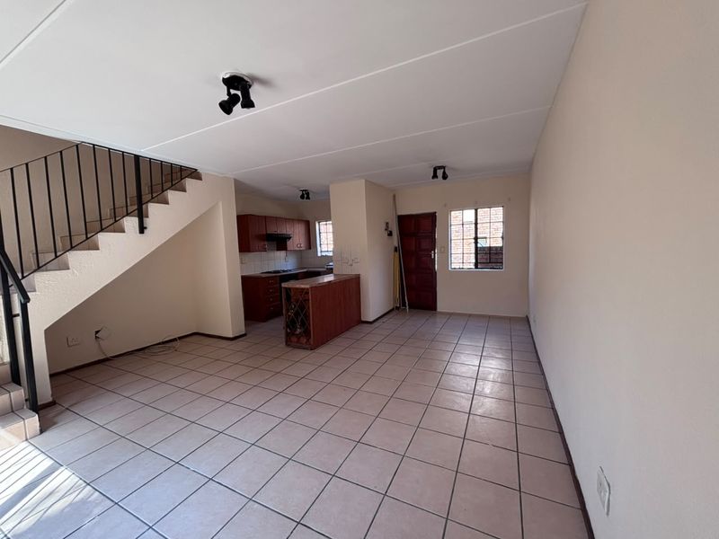 Spacious open-plan living and kitchen area featuring tiled flooring, a staircase with metal railing, and functional built-in cabinetry.
