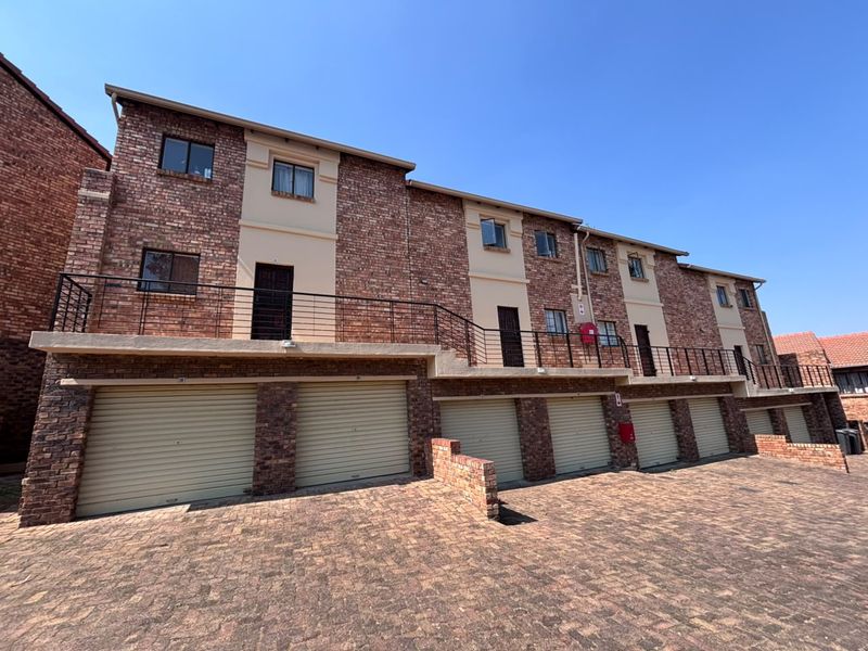 Front elevation of a multi-level townhouse complex featuring face brick construction, multiple roller shutter garage doors, and a shared upper-level balcony.