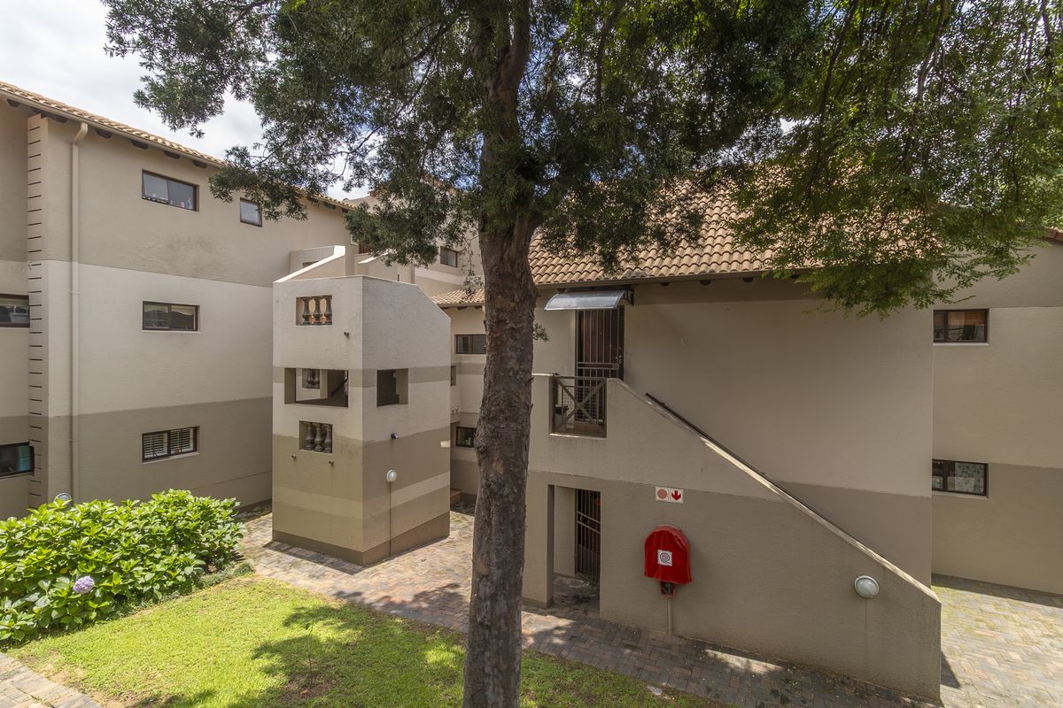 A view of the apartment complex exterior featuring a paved courtyard, staircase access, and established landscaping.