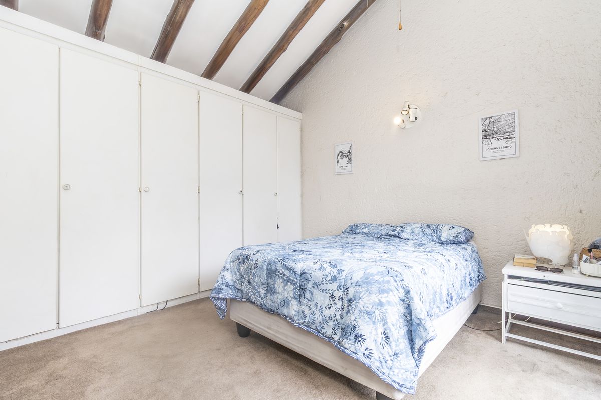 A bedroom featuring built-in cupboards, exposed timber ceiling beams, and a textured wall finish, offering a cozy and character-filled living space.