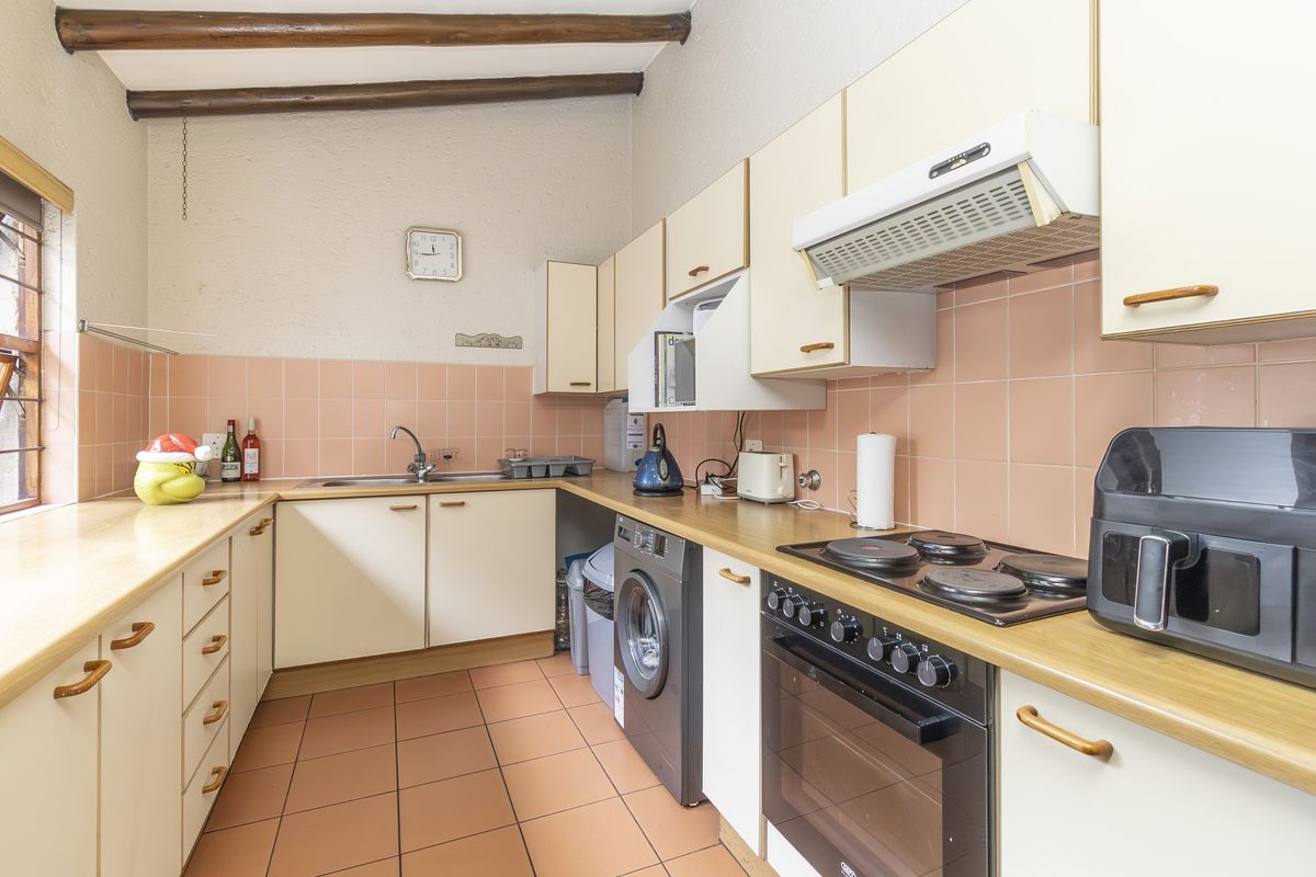 A functional kitchen featuring laminate countertops, built-in cabinetry, an electric oven and hob, and exposed timber ceiling beams with a tiled backsplash.