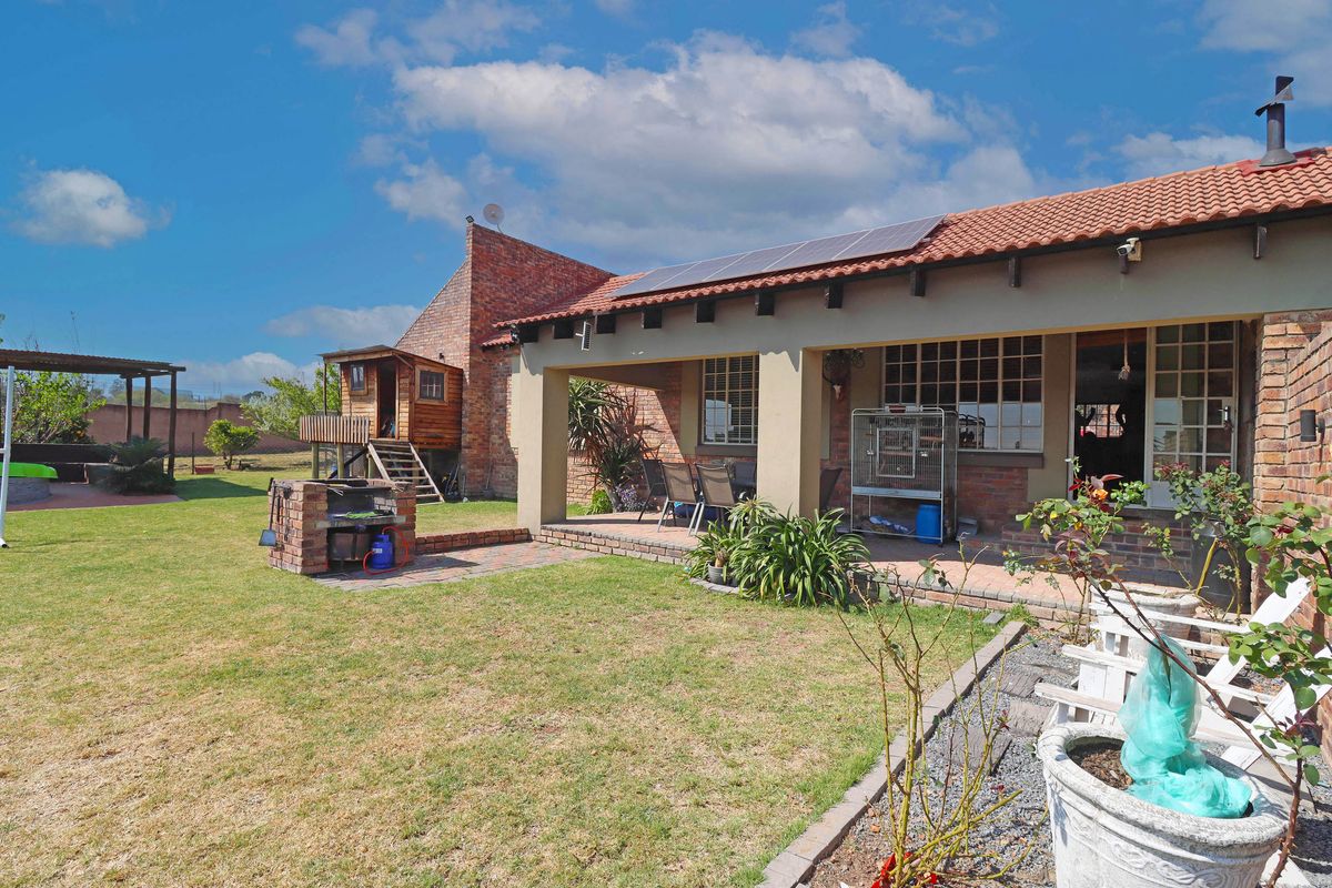 Rear view of the farm property featuring a covered patio, brick built-in braai, and solar panels installed on the tiled roof.